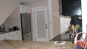 A kitchen with a refrigerator, a coffee maker, and a microwave. There is a door and a countertop with various items.