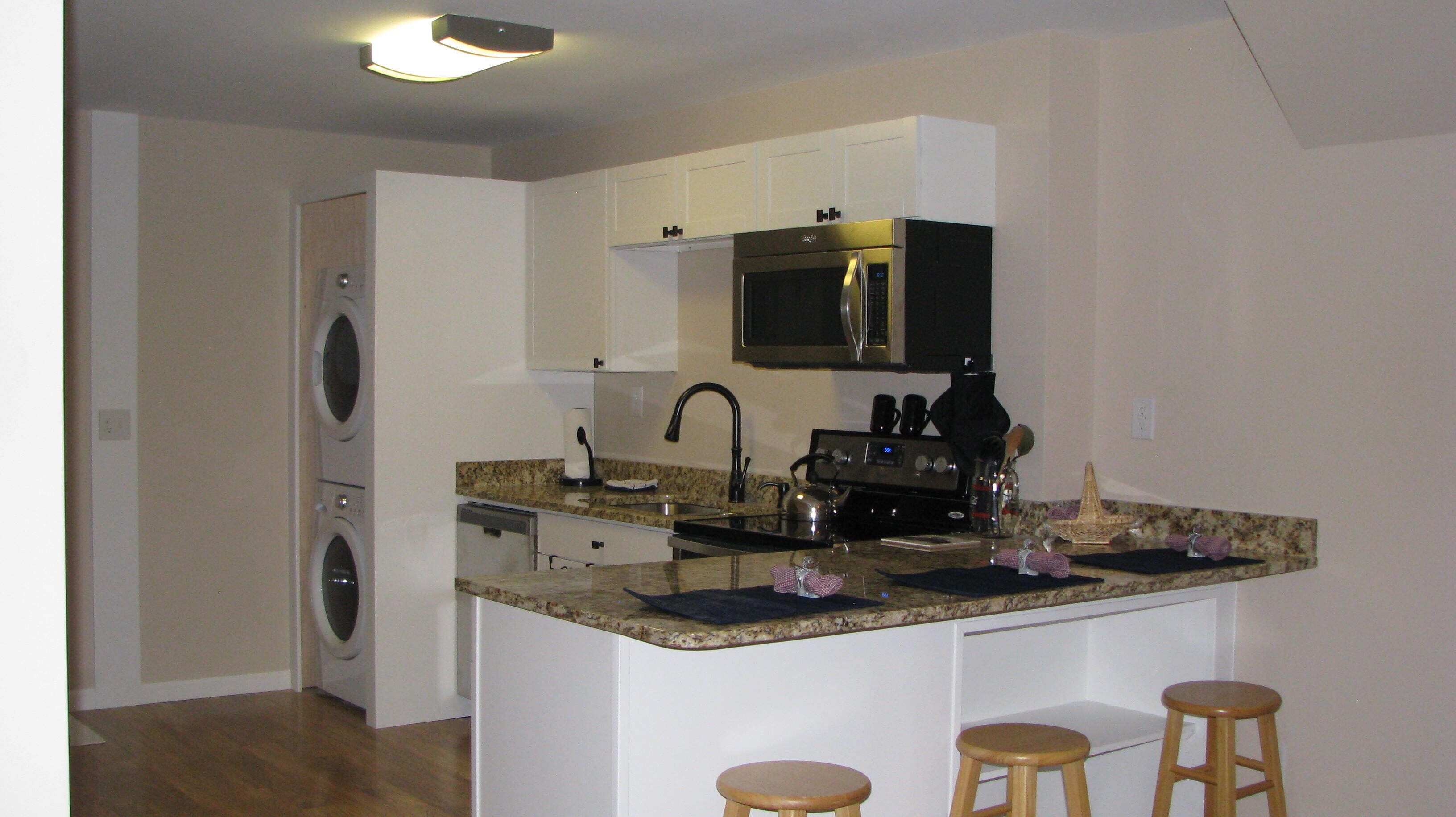 Cocina compacta con microondas, estufa y lavabo. Hay una lavadora en la habitación contigua.
