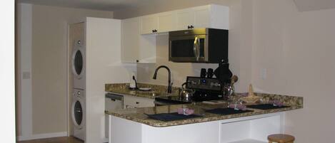 Cocina compacta con microondas, estufa y lavabo. Hay una lavadora en la habitación contigua.