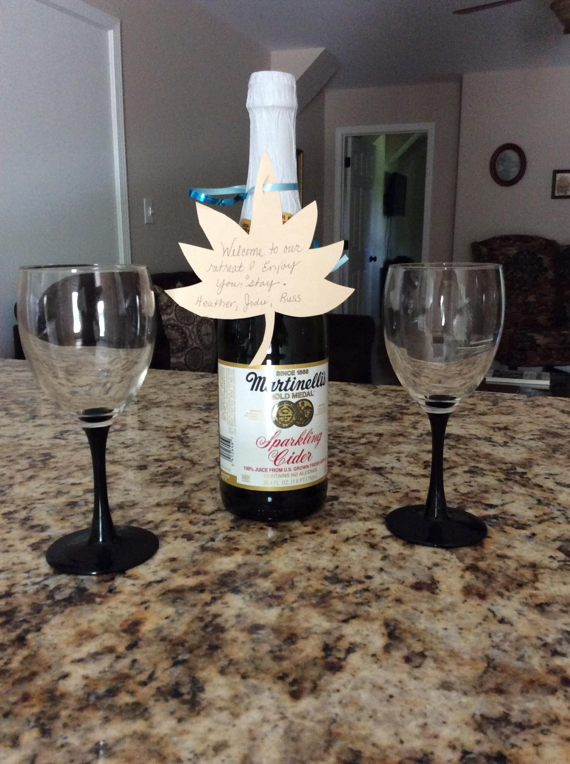 A bottle of sparkling cider on a kitchen counter with two empty wine glasses.
