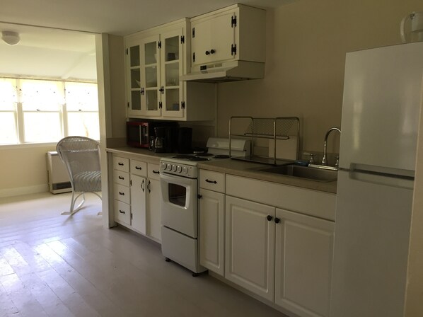A kitchen with white cabinets, a stove, an oven, a microwave, and a sink. - Lilac Cottage - Near Georgetown Island - Midcoast Maine (Arrowsic)