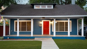 Ein eingeschossiges Haus mit roter Tür, weißen Säulen und blauer Außenfassade.