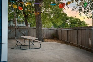 A concrete patio with a picnic table, surrounded by a wooden fence and trees.