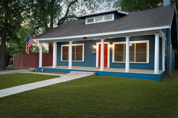 A single-story house with a porch, a red door, and an American flag.