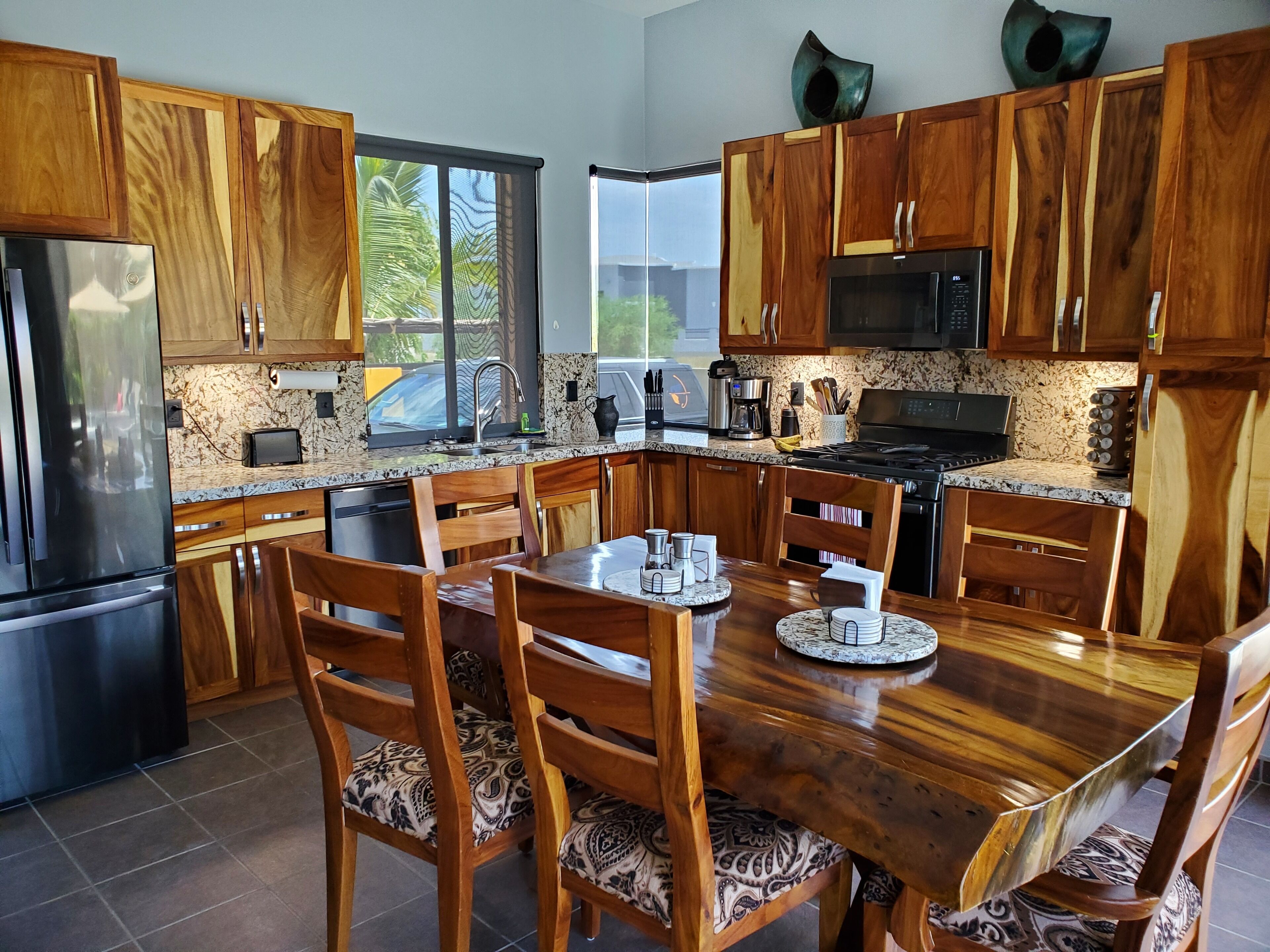 A modern kitchen with wooden cabinets, a stainless steel refrigerator, a microwave, and a dining area with a wooden table and chairs.