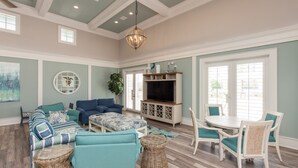 A spacious living room with a large TV, comfortable seating, and a dining area with white chairs. - Beachy Keen Platinum Property with Unbeatable View!   (Palm Coast)