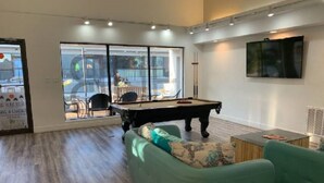 A modern living room with a pool table, green sofas, and large windows offering a view of the outside. - 3 bedrooms. 4 TV's. Great view, Nice Reviews. (St. George)