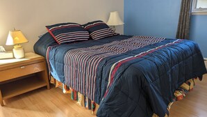 Un lit avec une couette à rayures, deux oreillers, une lampe de chevet et une table de chevet.