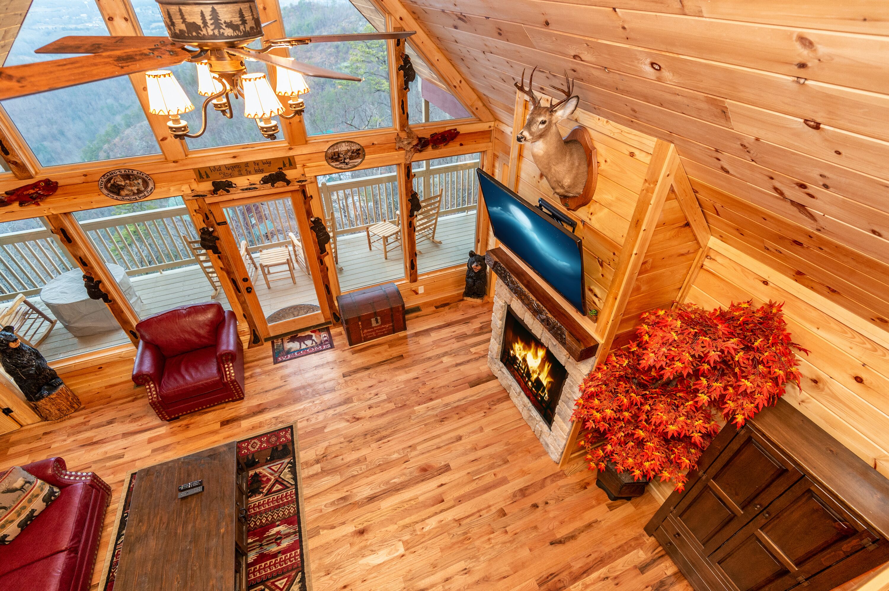 A log cabin interior with a fireplace, wooden floors, a mounted deer head, and a television.