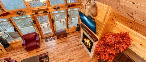 A log cabin interior with a fireplace, wooden floors, a mounted deer head, and a television.