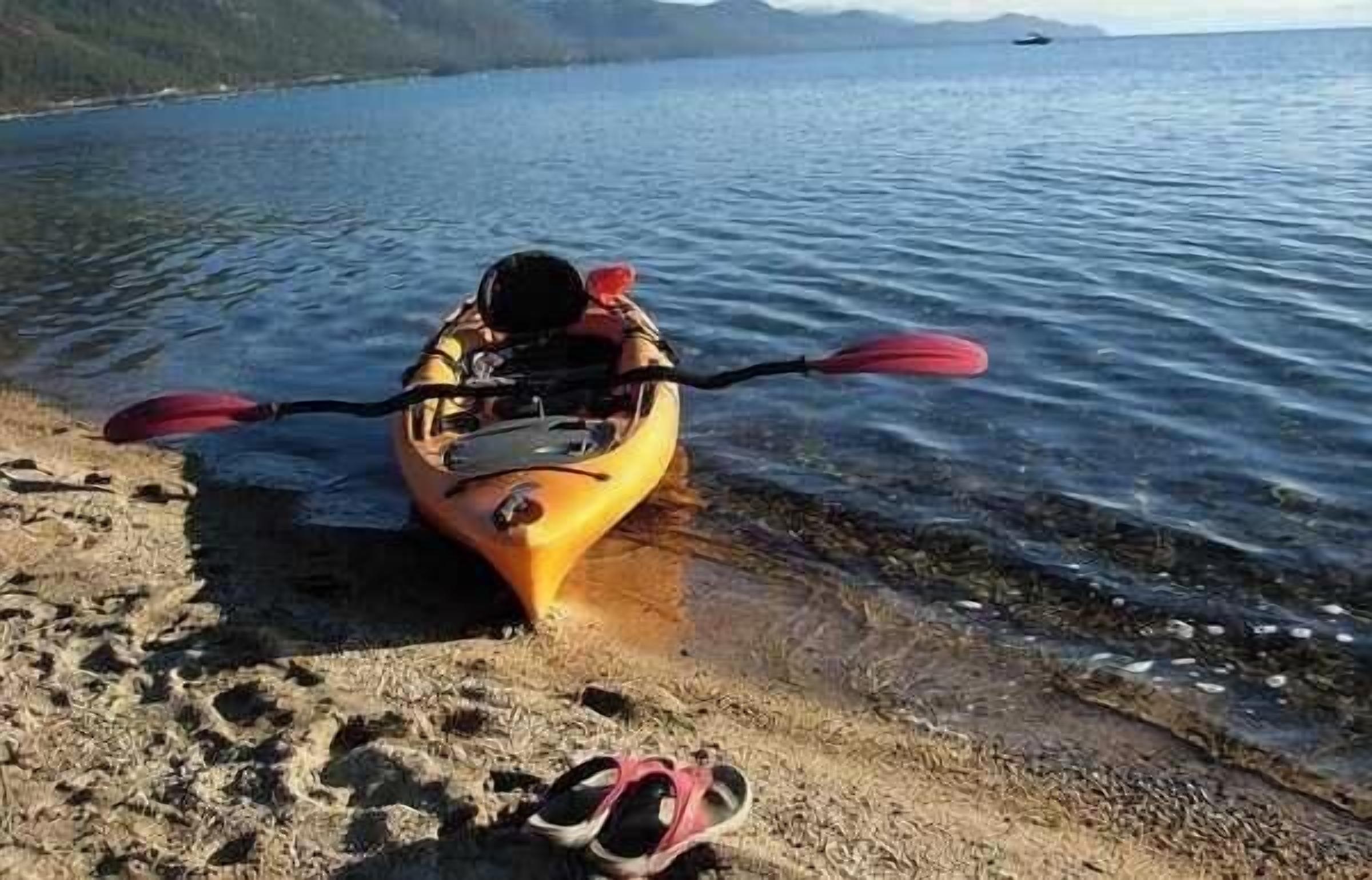 A kayak on a sandy shore with a pair of shoes nearby.