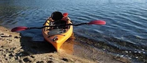 A kayak on a sandy shore with a pair of shoes nearby.