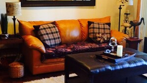 Een woonkamer met een bruine leren bank, een zwarte salontafel en een wit pluisachtig vloerkleed.