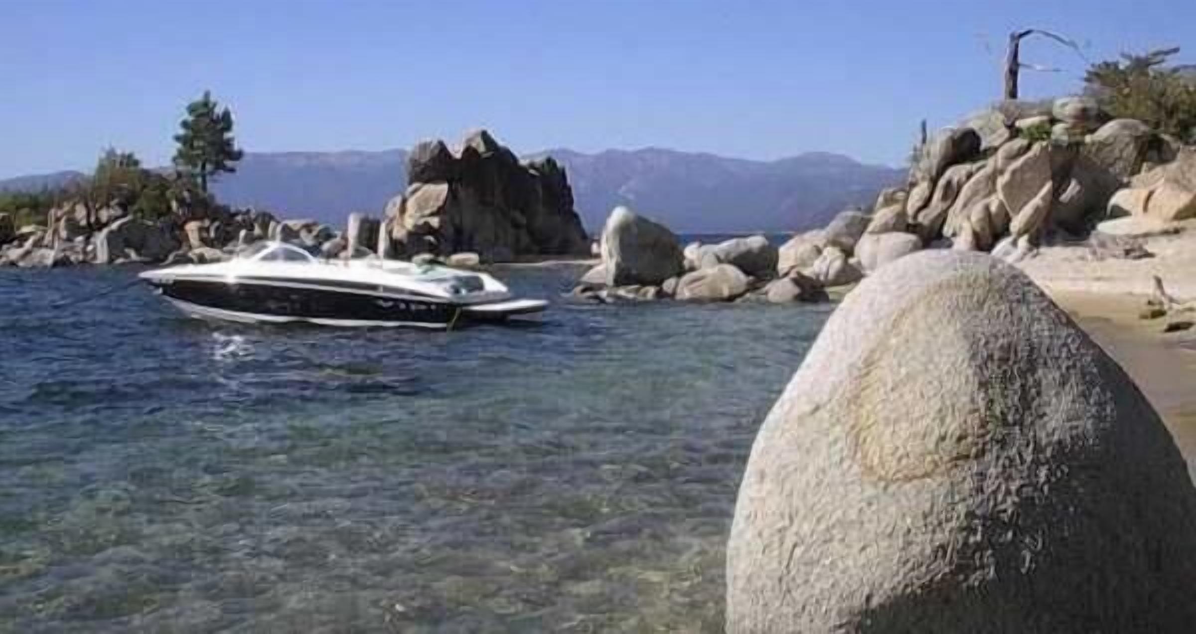 A boat on clear water near rocky shores with mountains in the background.