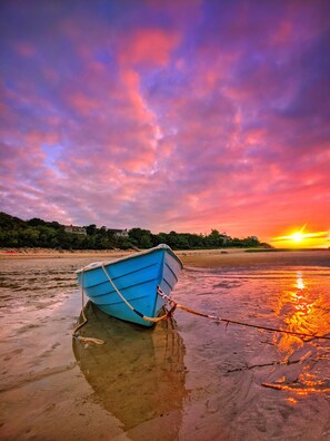 A blue boat tied to a dock on a beach with a sunset in the background.