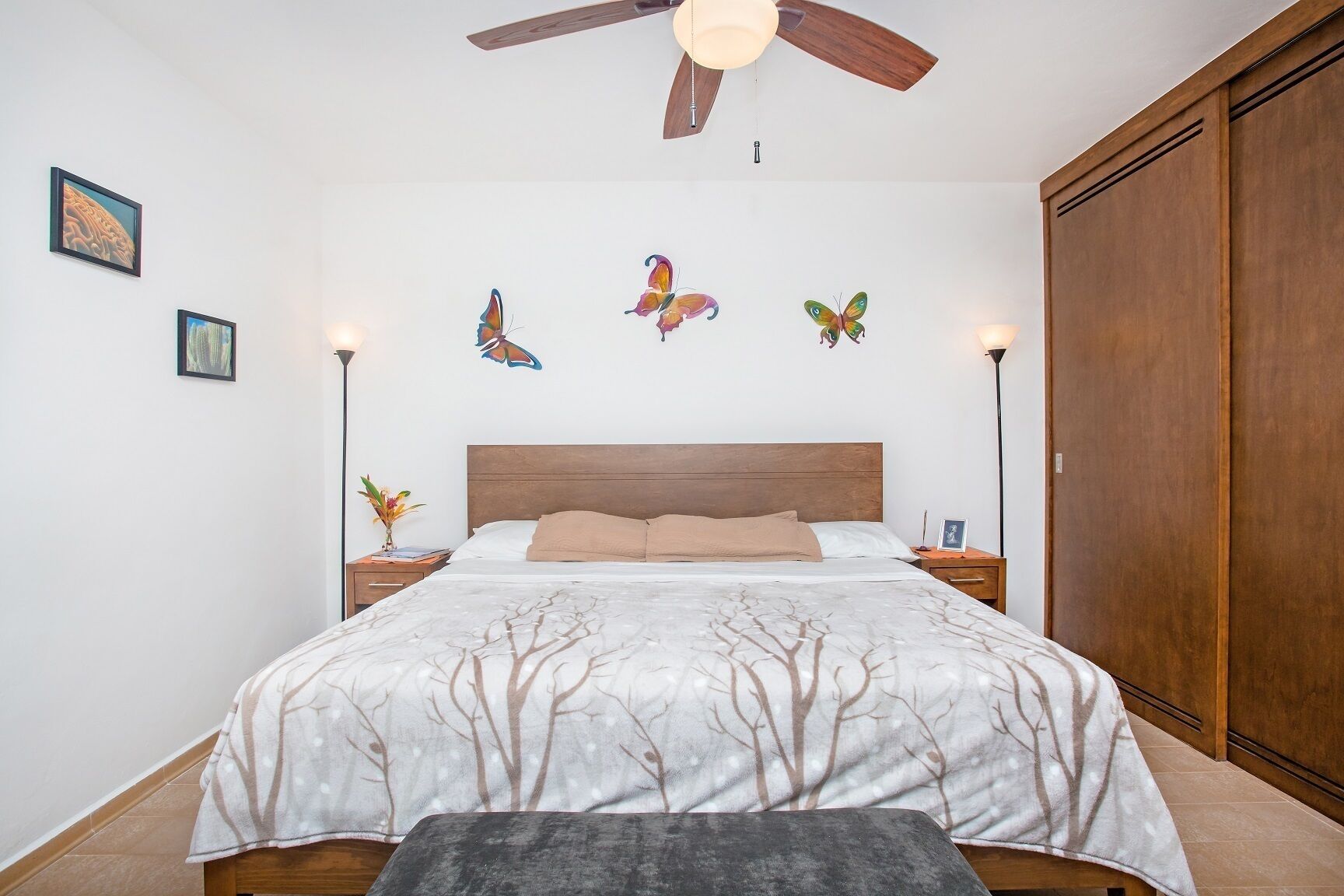 A bedroom with a bed, a ceiling fan, wall art, and a wardrobe.