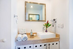 A bathroom with a sink, mirror, towel rack, and a hairdryer mounted on the wall. - Oceanfront condo on the bluest ocean of Cozumel island (Cozumel)