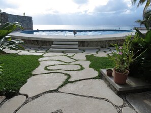 A pool with a stone border and steps leading to it, surrounded by a garden with a patterned walkway. - Oceanfront condo on the bluest ocean of Cozumel island (Cozumel)