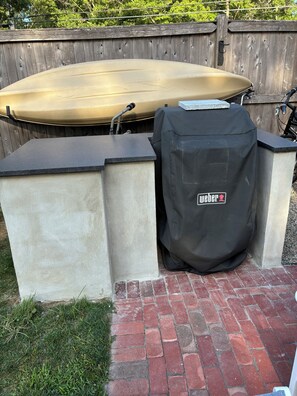Una parrilla para barbacoa y una funda protectora junto a un muro de ladrillo.