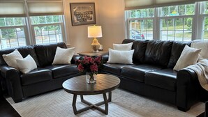 A living room with two black leather sofas, a round coffee table, and a vase with flowers.