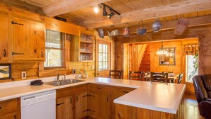 A wooden cabin interior with a kitchen featuring wooden cabinets, a white countertop, and a dishwasher. - Gorgeous, Secluded, SuperFast WiFi, NFL Sunday, Arcade, Gated, Fishing & 2 Pools (Sevierville)
