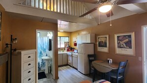 A compact kitchen with a dining area, a ceiling fan, and two framed artworks on the wall.