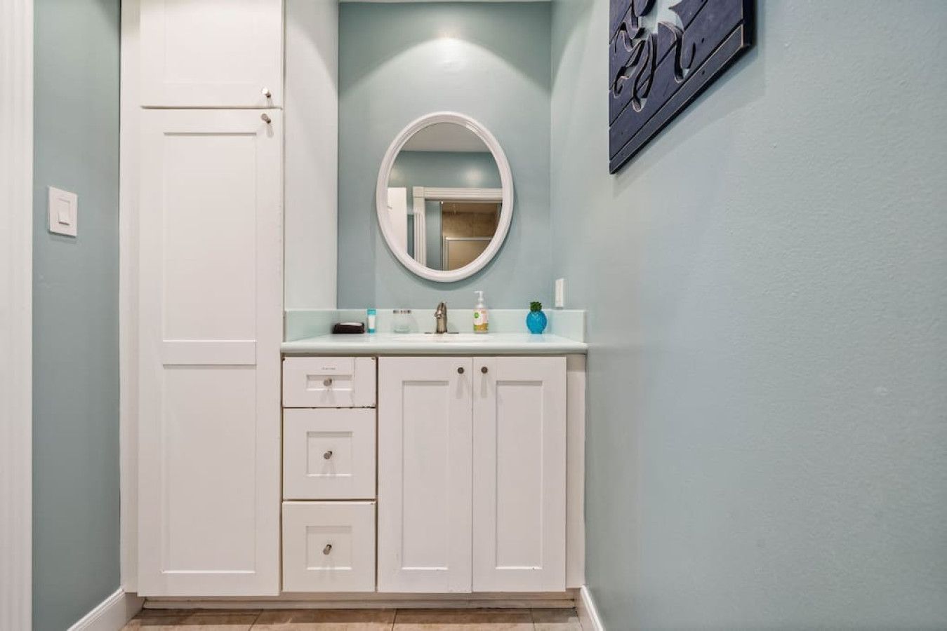 Une salle de bain avec un meuble-lavabo blanc, un miroir rond et un mur bleu clair.
