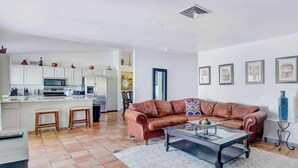 A living room with a brown leather sofa, a glass coffee table, and a kitchen area with white cabinets and a microwave. - Luxury 5BR | Private Pickleball, Pool, Spa (Scottsdale)