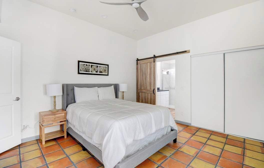 Une chambre à coucher comprenant un lit, des tables de chevet, un ventilateur de plafond, une armoire et un sol carrelé.