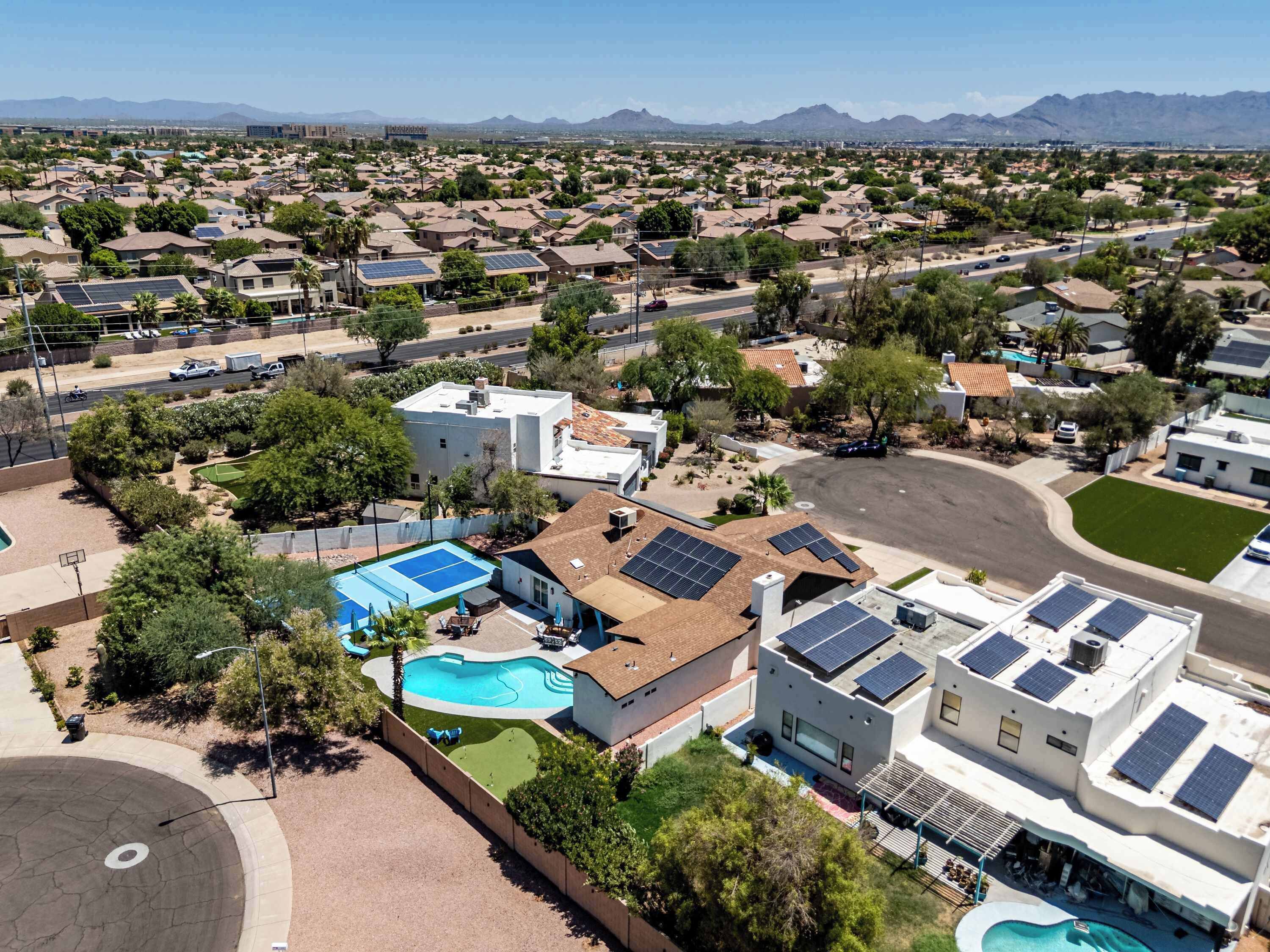 Un quartier résidentiel avec des maisons, des panneaux solaires, une piscine et une vue dégagée sur les montagnes lointaines.