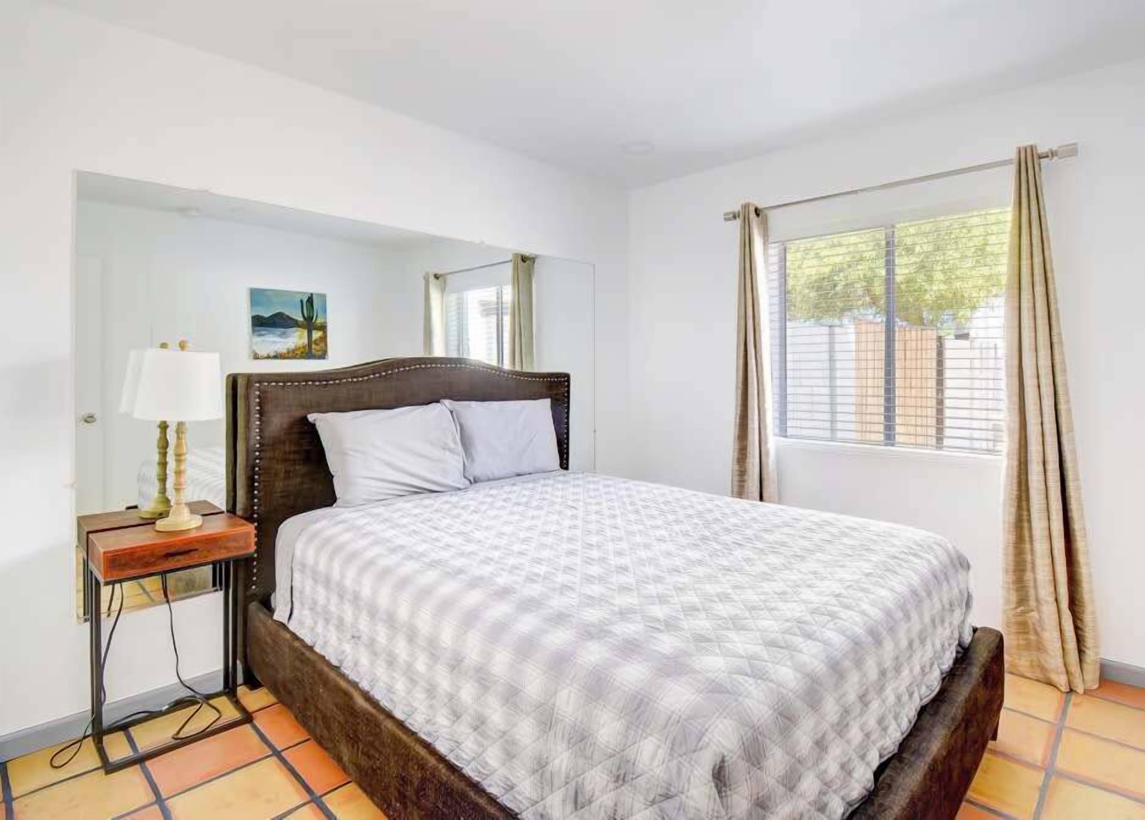 A neatly made bed with a patterned bedspread, a bedside table with a lamp, and a window with curtains.