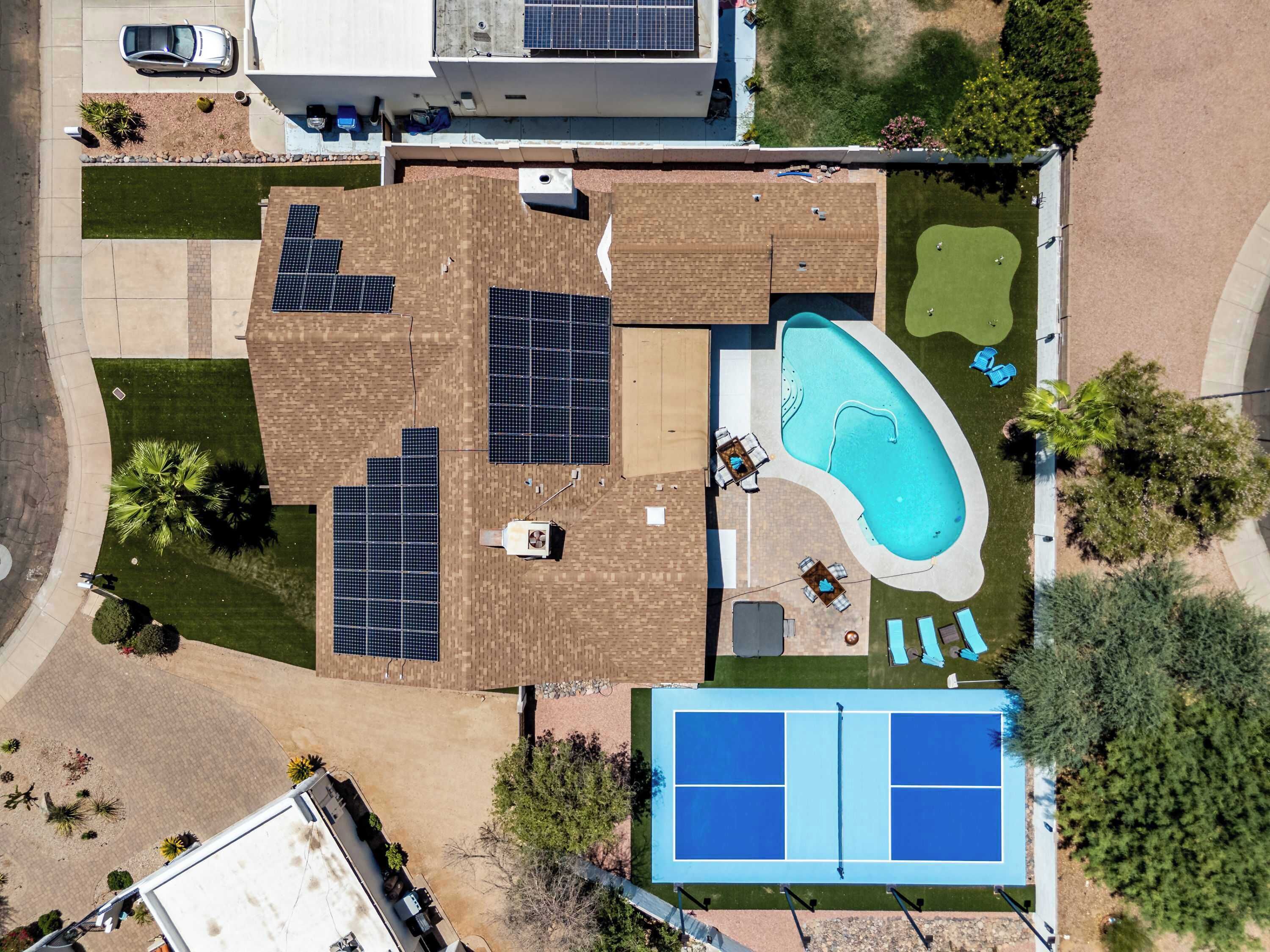 A residential property with a swimming pool, solar panels, a tennis court, and a covered patio area.