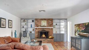 A living room with a brick fireplace, leather sofa, and shelves with decorative items. - Luxury 5BR | Private Pickleball, Pool, Spa (Scottsdale)