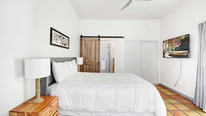 A hotel room with a bed, a wooden nightstand, a ceiling fan, a TV, and a sliding door. - Luxury 5BR | Private Pickleball, Pool, Spa (Scottsdale)