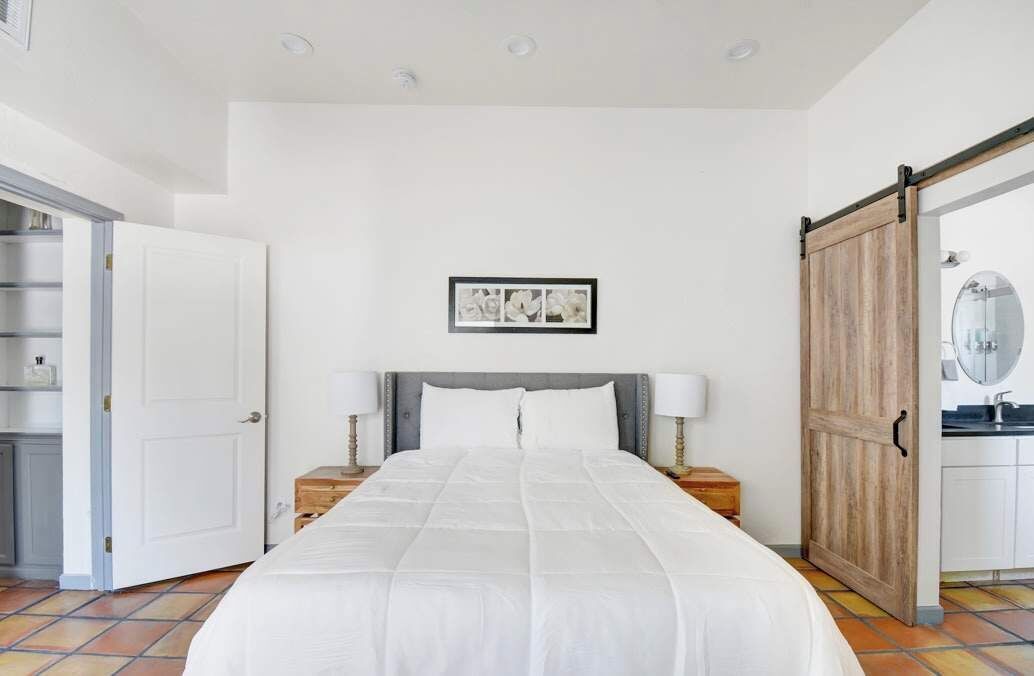 A bedroom with a large bed, a wooden sliding door, a white wall, and a framed picture above the bed.