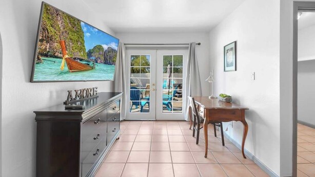A room with a large TV on the wall, a dining table with chairs, and a view of a beach through a glass door. - Luxury 5BR | Private Pickleball, Pool, Spa (Scottsdale)