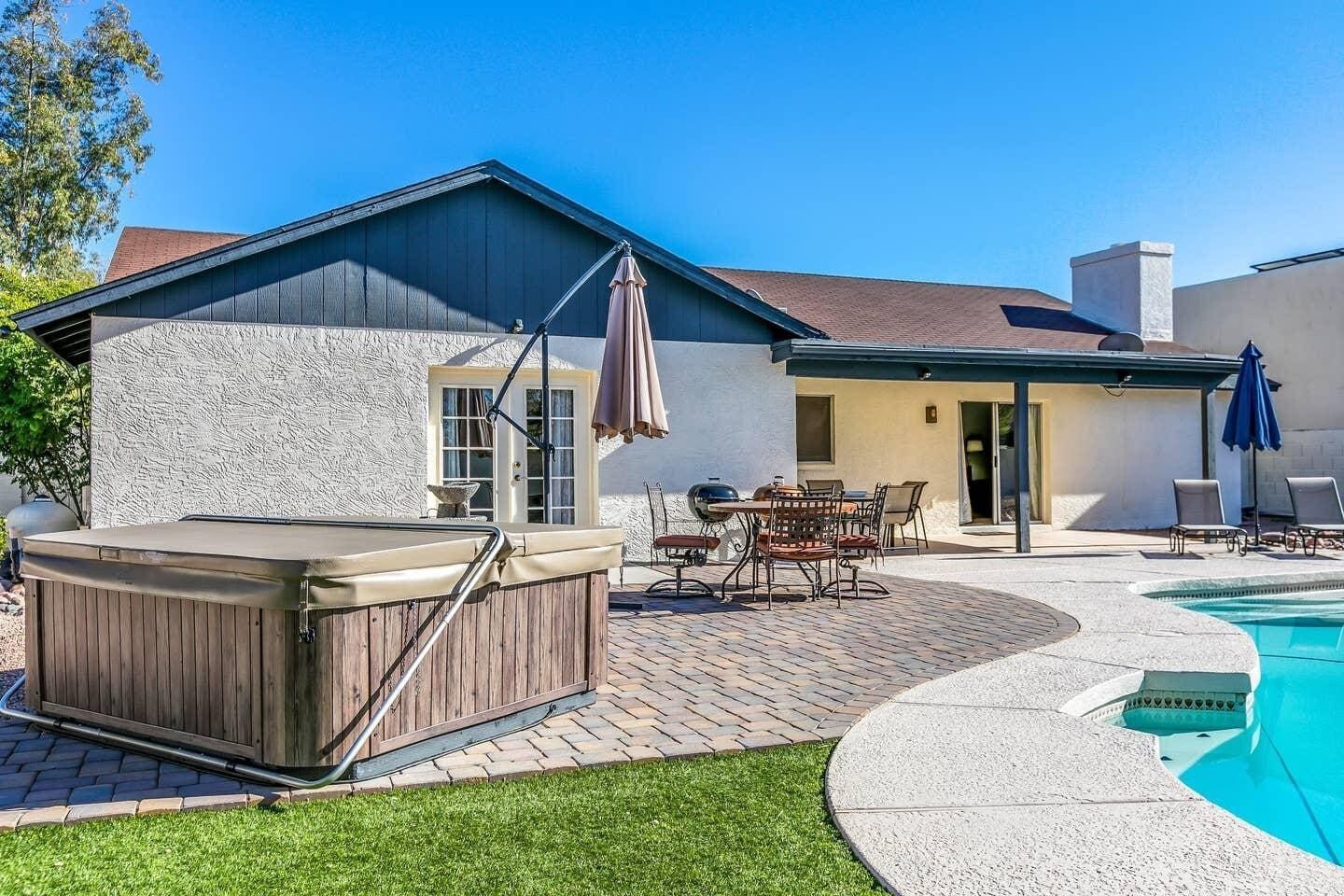 A backyard with a hot tub, patio furniture, and a swimming pool.