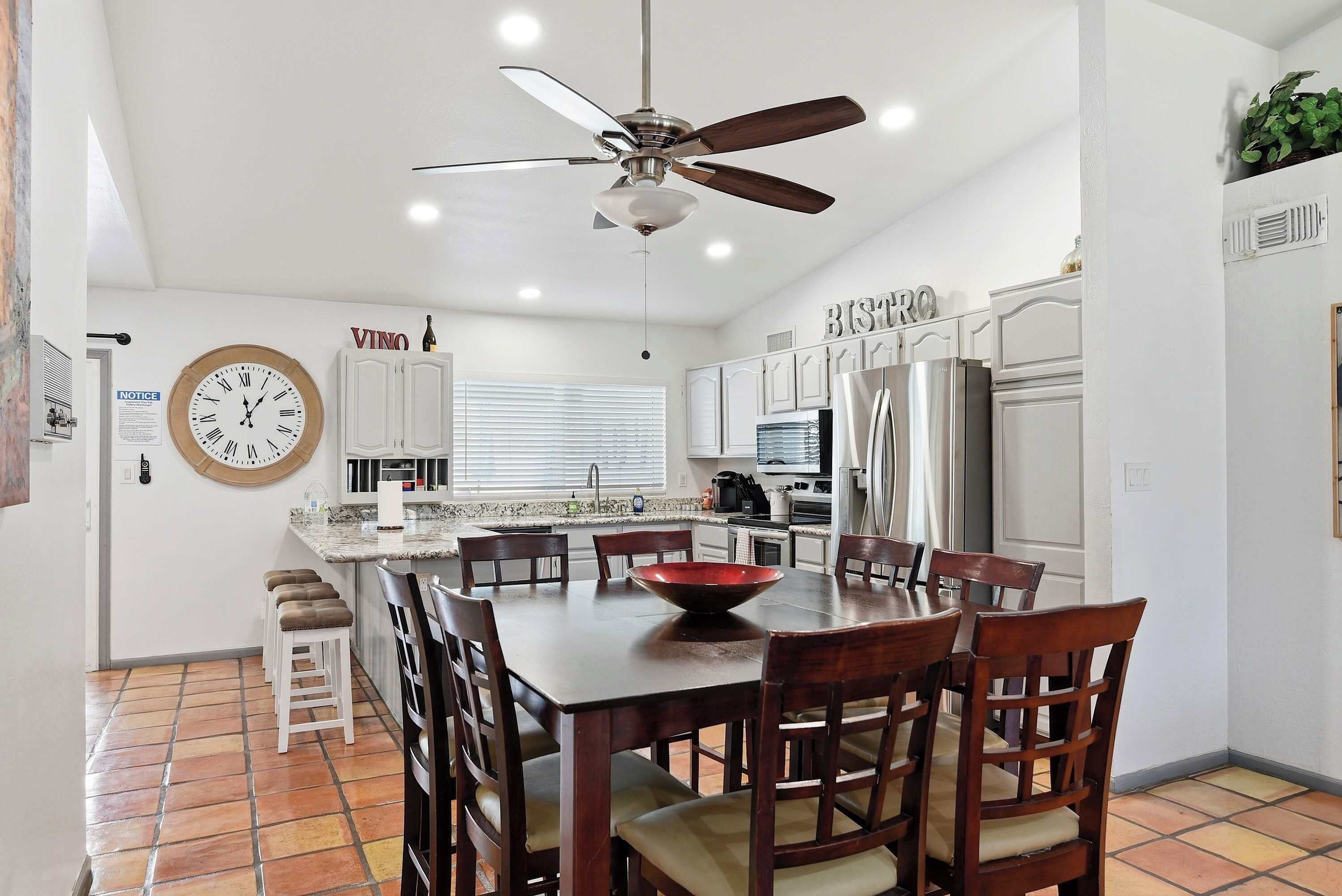 A modern kitchen with a central island, white cabinetry, and a dining area with wooden chairs.