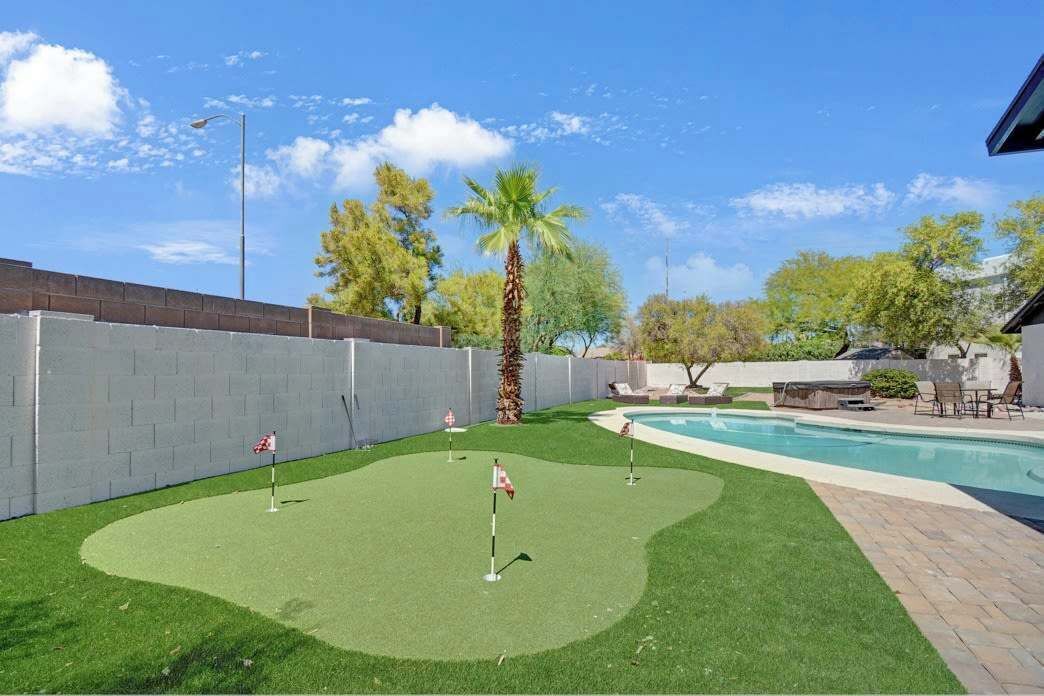 Un jardin avec une piscine, une pelouse artificielle, des palmiers et un mur en briques.