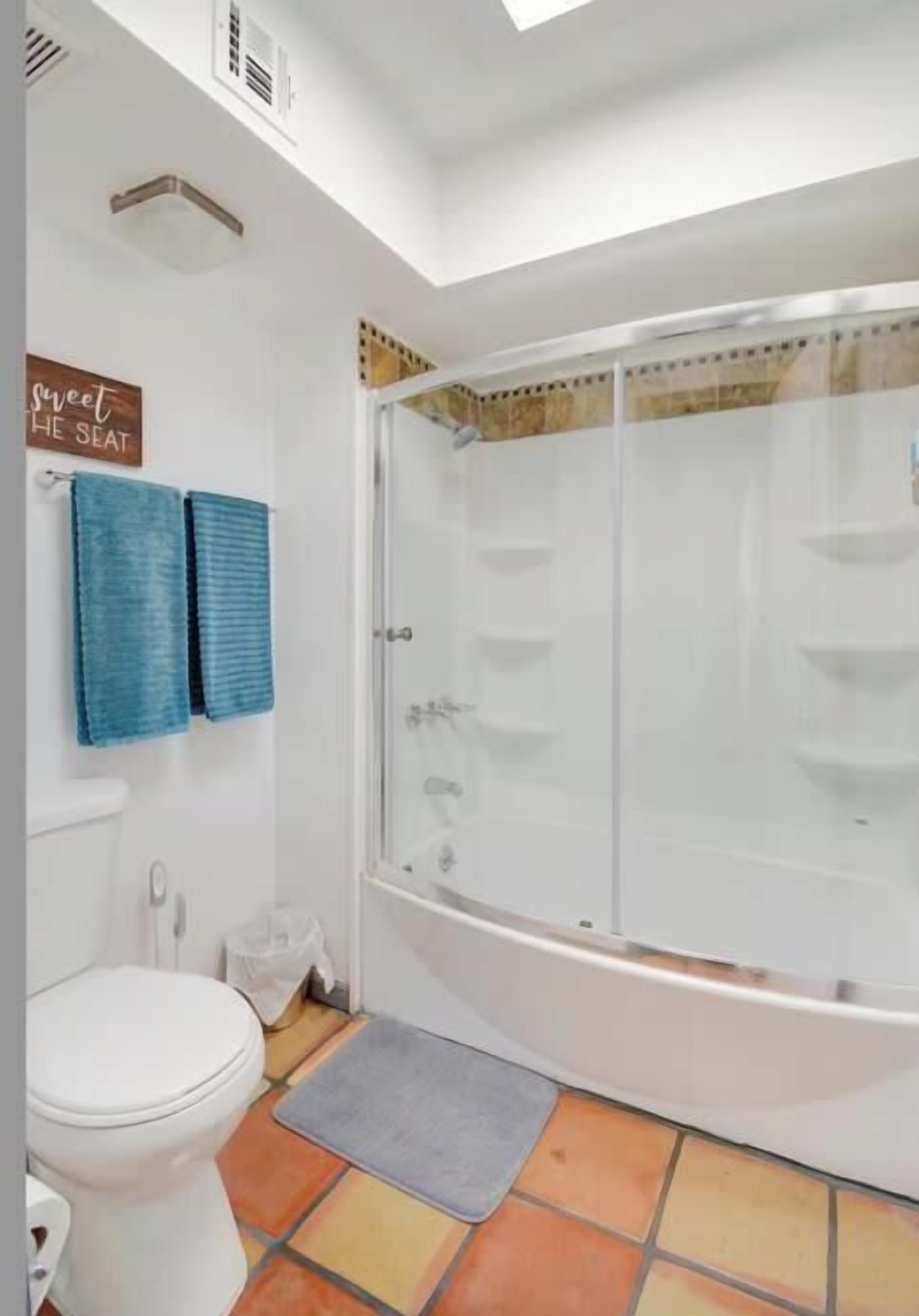 Une salle de bain avec des toilettes blanches, une douche dotée d’une porte en verre et un sol carrelé aux couleurs vives.