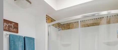 Une salle de bain avec des toilettes blanches, une douche dotée d’une porte en verre et un sol carrelé aux couleurs vives.