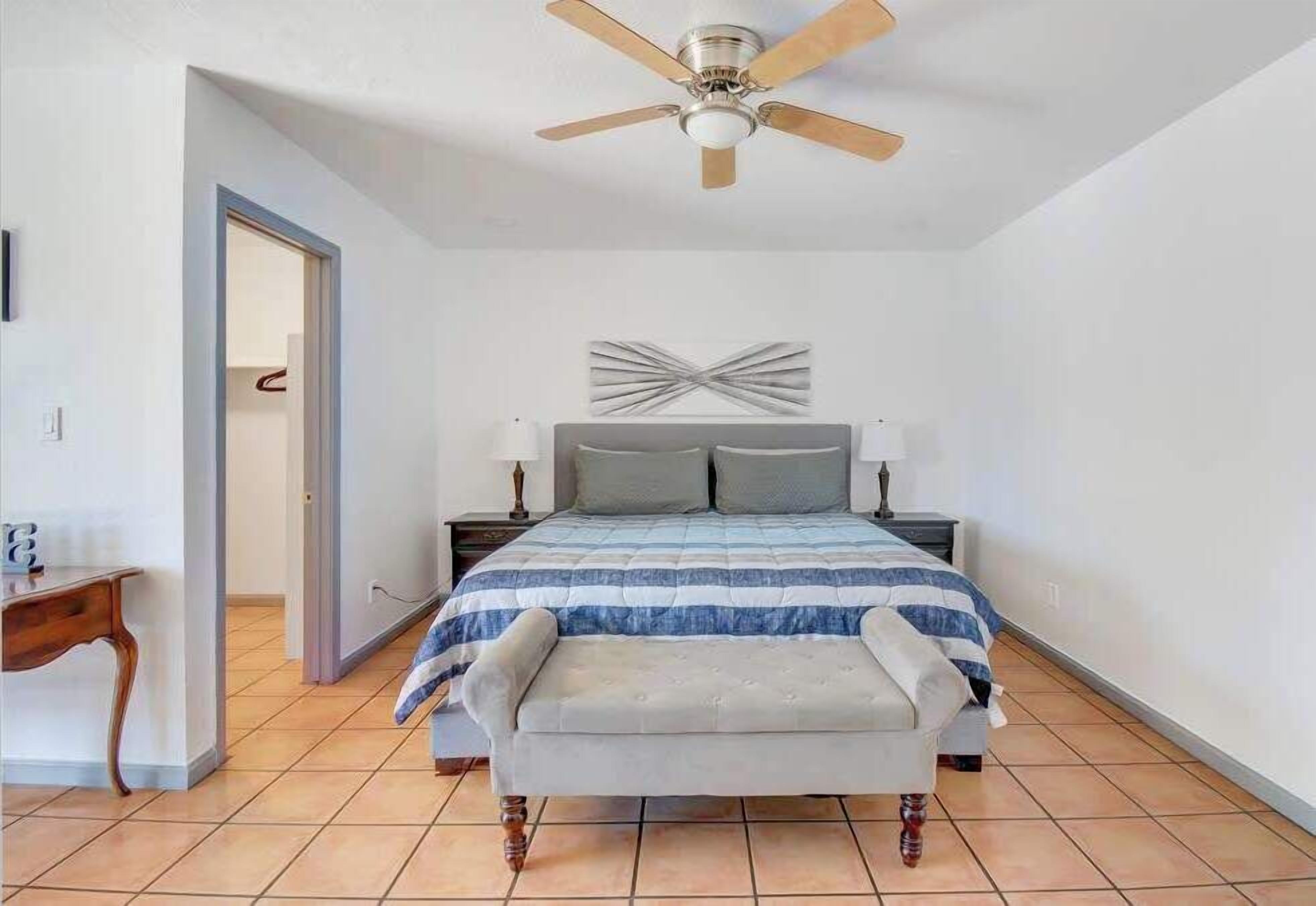 Ein Schlafzimmer mit Bett, einer Bank, einem Deckenventilator und einer Wandleuchte.