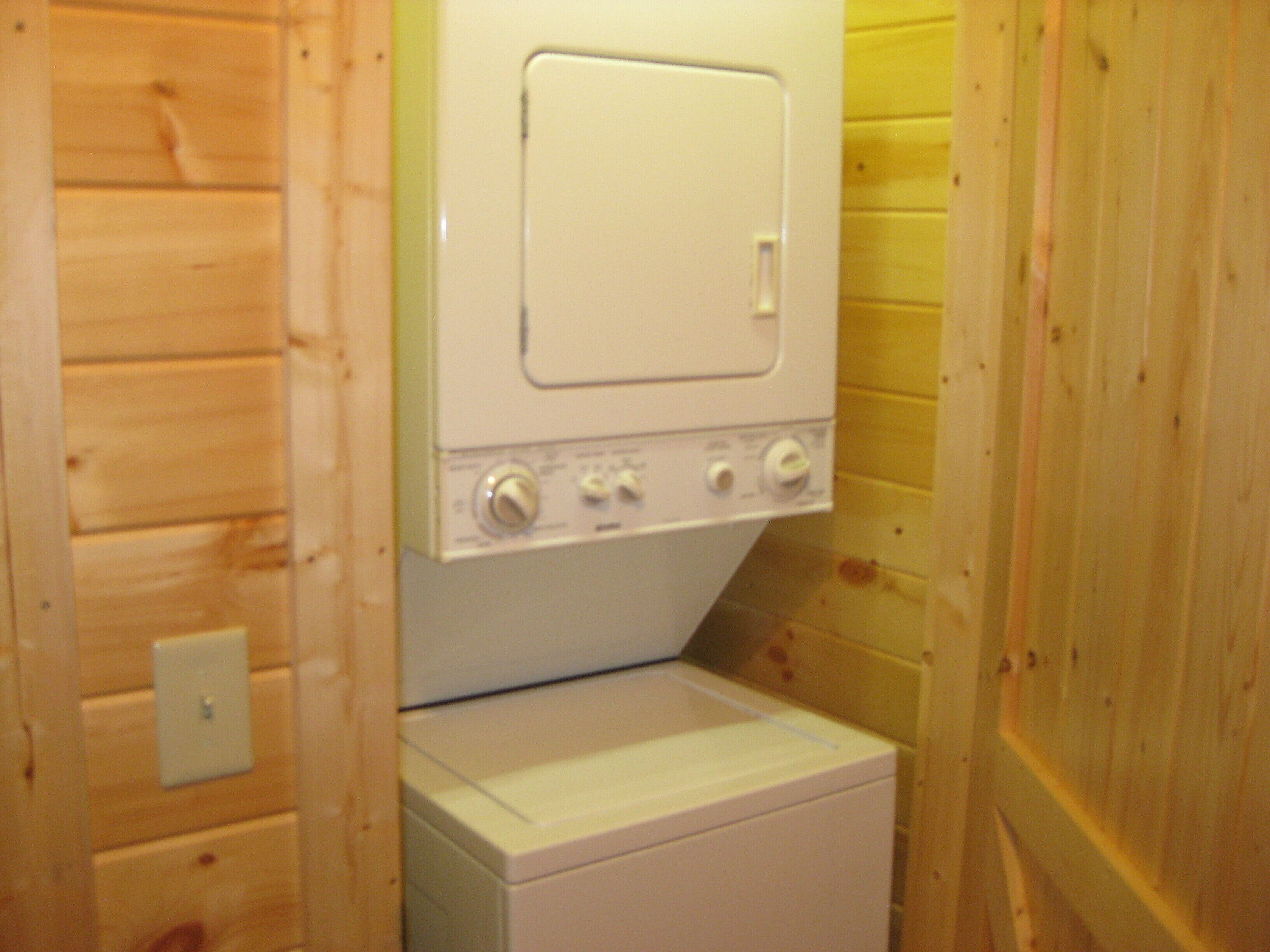 Une petite buanderie avec un lave-linge et un sèche-linge blancs, des murs en bois et un interrupteur situé à gauche.