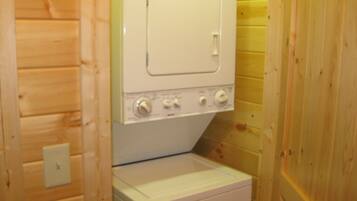 Une petite buanderie avec un lave-linge et un sèche-linge blancs, des murs en bois et un interrupteur situé à gauche.