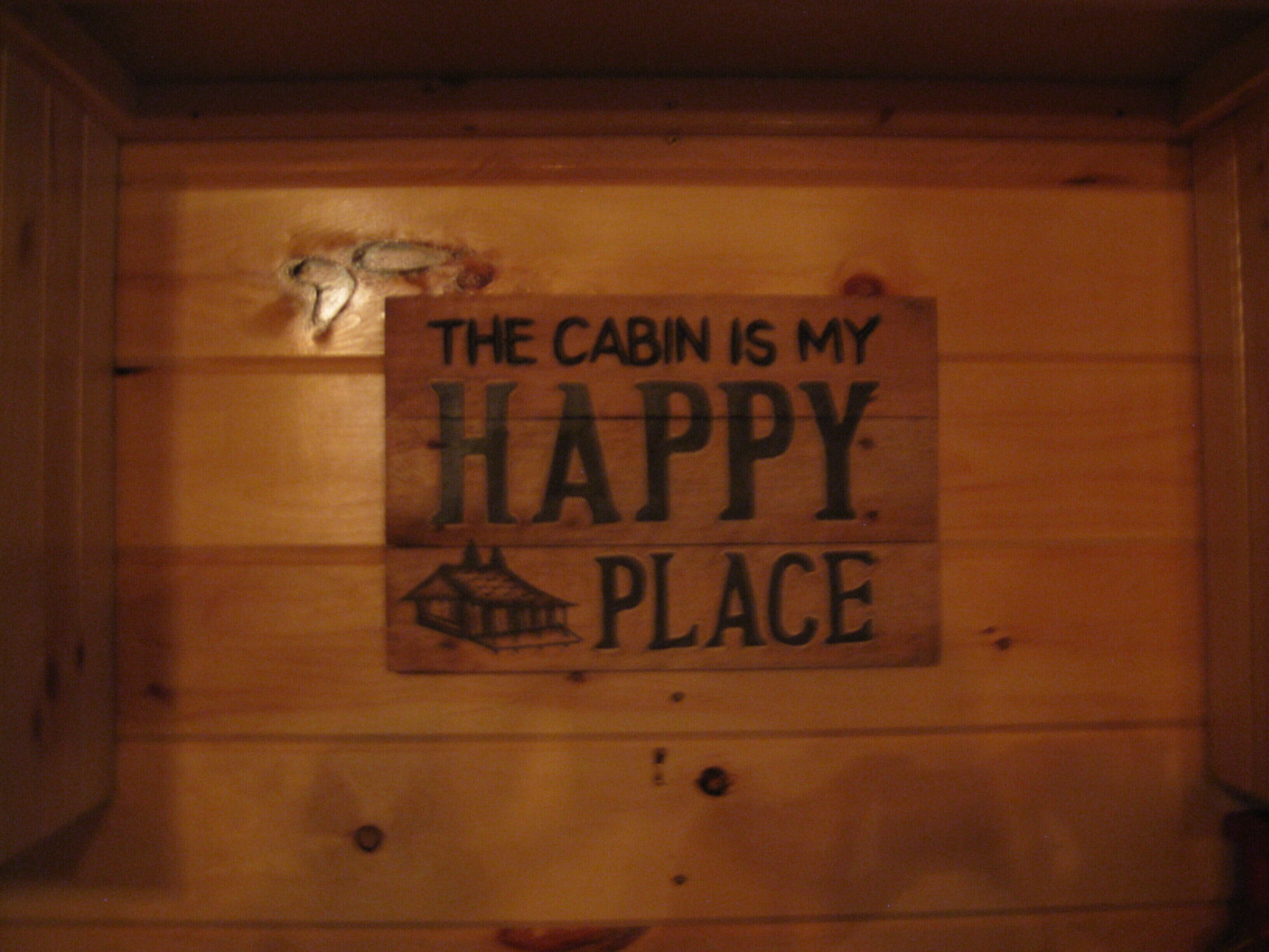 L'interno di una baita in legno, con un cartello che recita: 'THE CABIN IS MY HAPPY PLACE'.