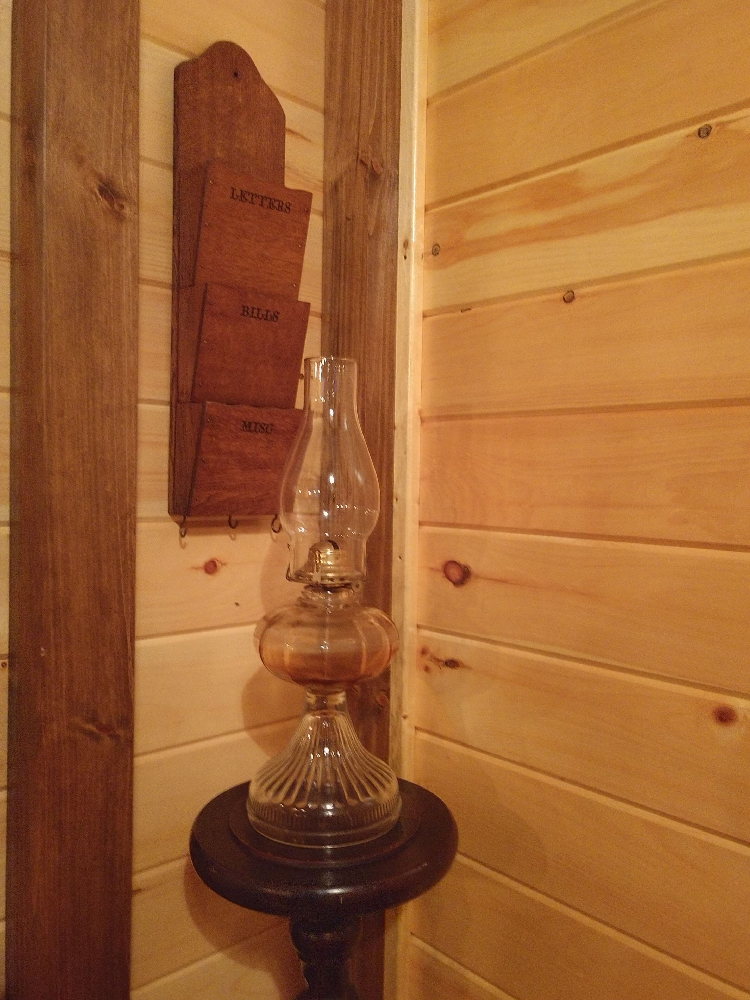 Eine Holzwand mit einem angebauten Holzschild und einer klaren Glaslampe auf dunklem Fuß.