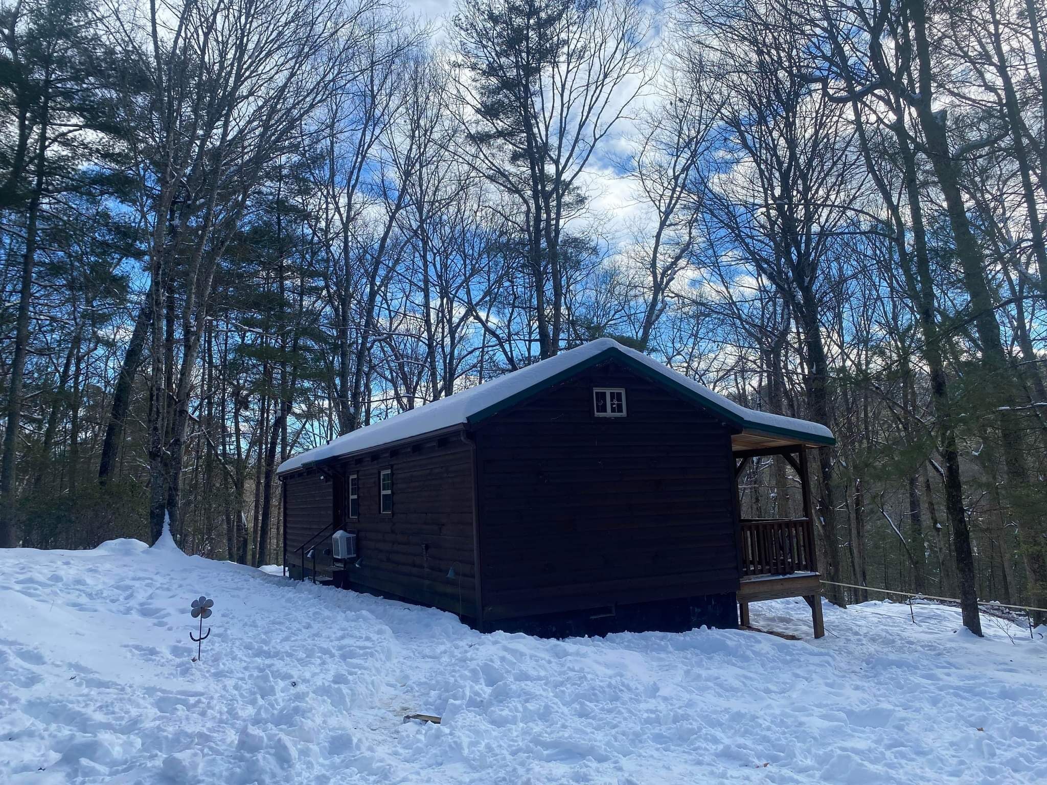 A wooden cabin with a porch, surrounded by snow and trees.