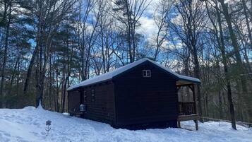 A wooden cabin with a porch, surrounded by snow and trees.