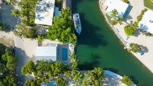 Vista aérea de uma propriedade costeira com piscina, um barco atracado na água e vários edifícios com design moderno.