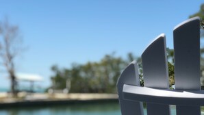 Uma cadeira Adirondack branca voltada para um corpo d'água, com céu claro.